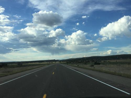 View of a two-lane highway in the desert with blue sky and clouds