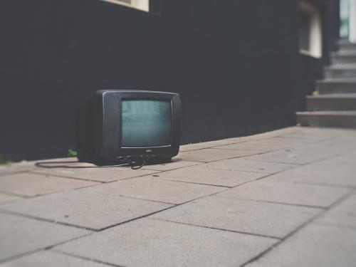 Horizontal close up of a black tv sitting on the ground. 